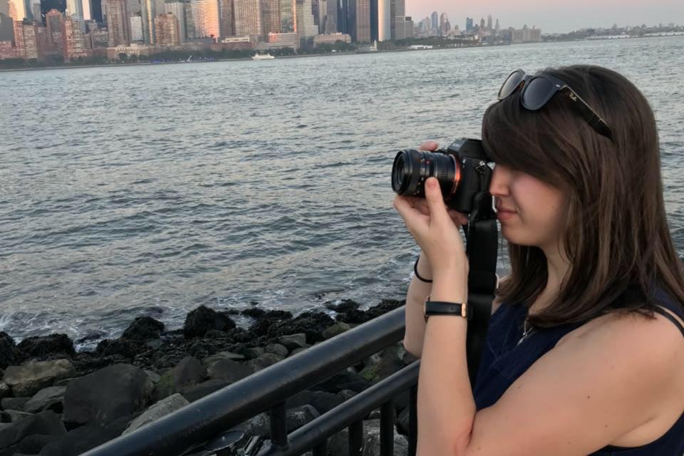 A woman holding a camera pointed toward the New York City skyline