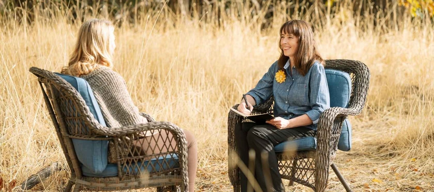 a woman sitting in a chair in a field listening to another women