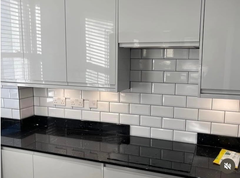 Modern white gloss kitchen cabinets with white subway tile backsplash and black granite countertops.