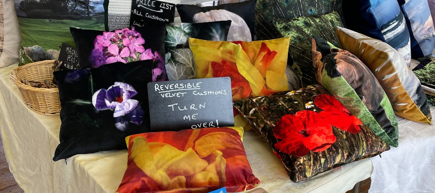 a selection of various handmade velvet cushions with nature photo prints on a craft stall display