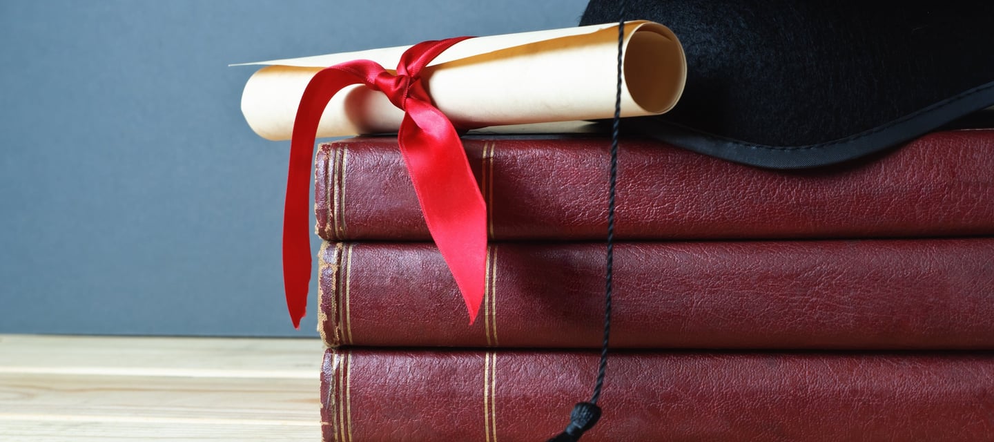 Stack of red books with a diploma, tied with a red ribbon, and a graduation cap on top