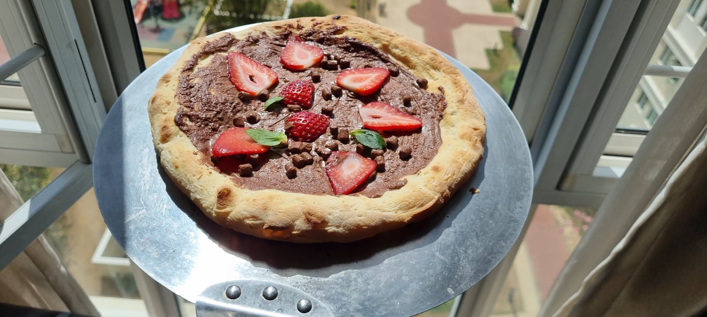 Homemade dessert pizza with chocolate hazelnut spread, fresh strawberry slices, and chocolate chips.