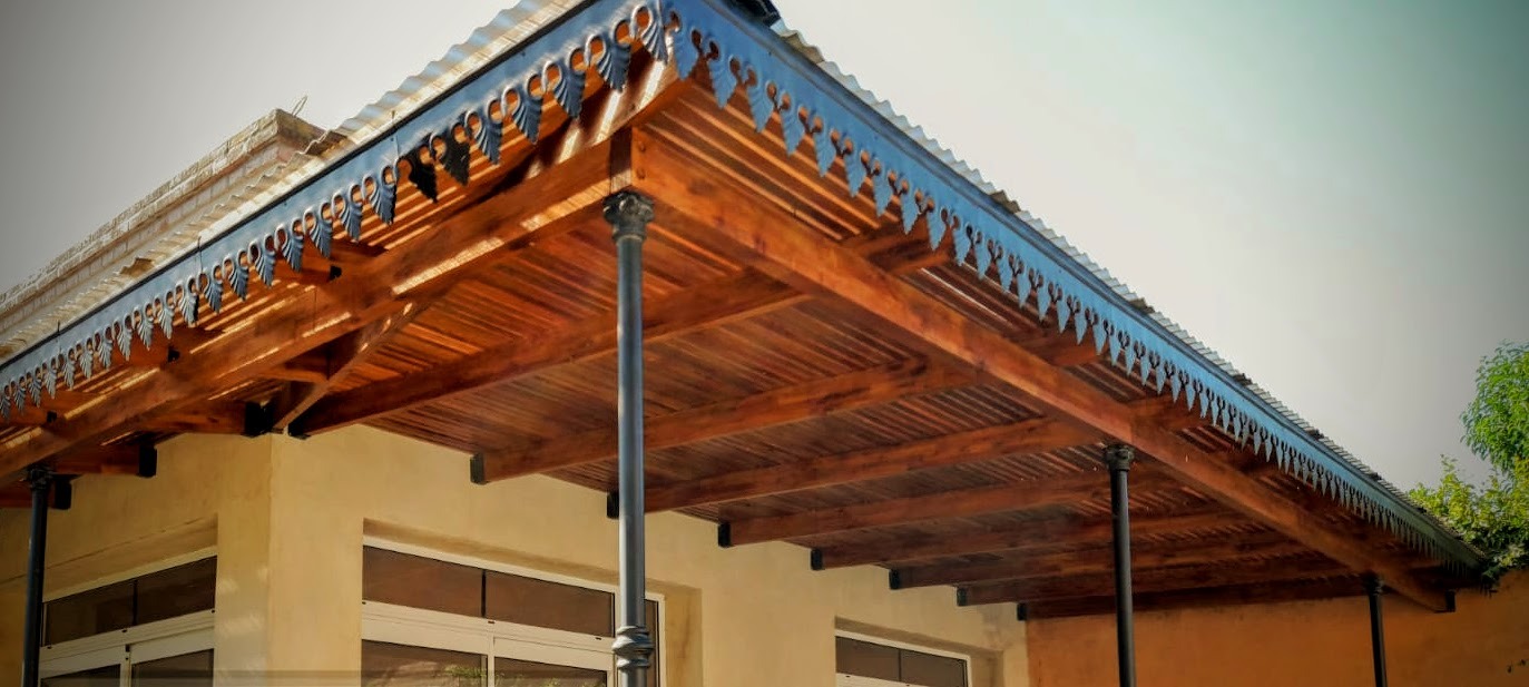 Toldo rústico de madera para porche con detalles decorativos de celosía y pilares de soporte negros.