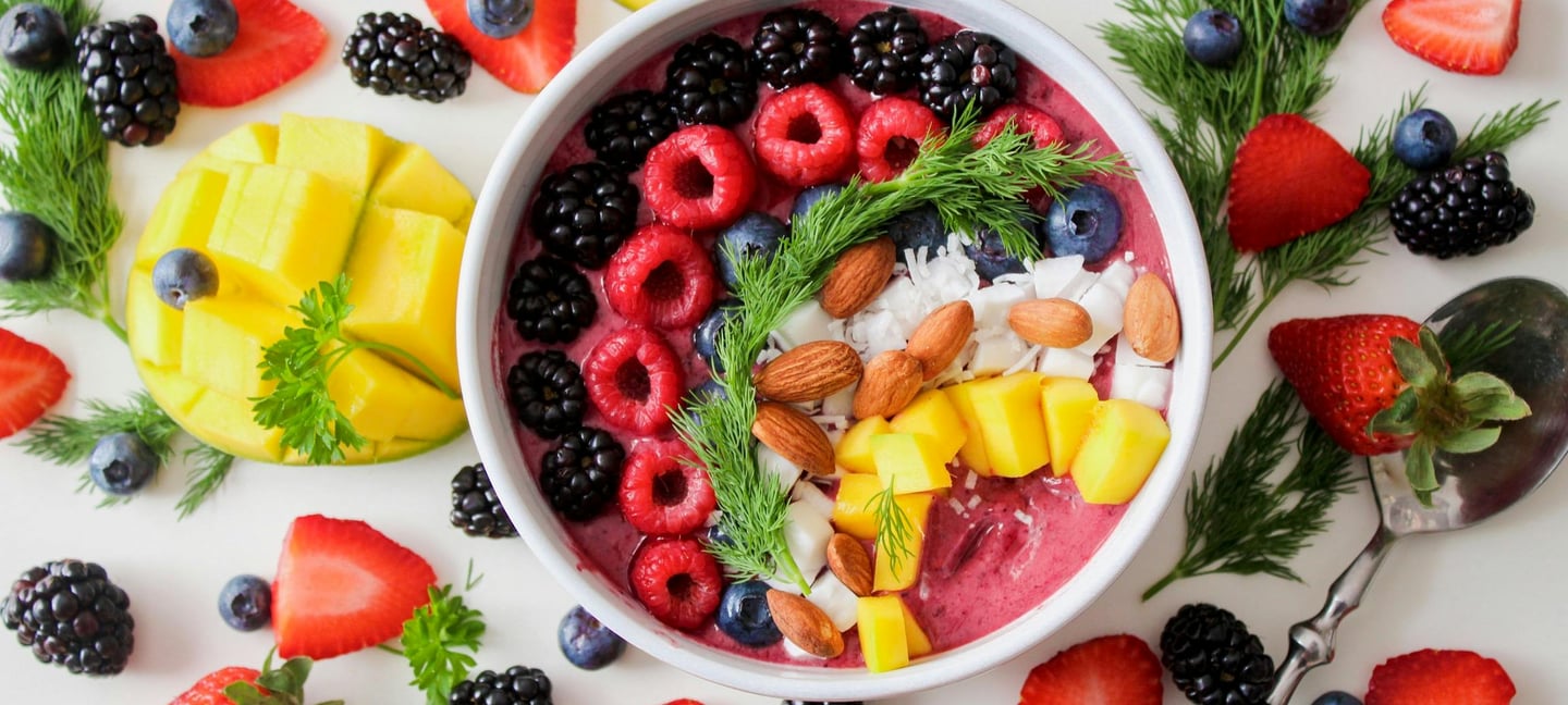 En la imagen está un plato saludable de comida que incluye, yogurt, bayas, almendras y frutos rojos