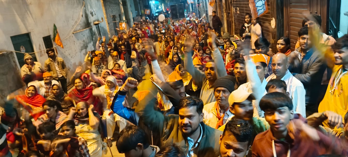 A large crowd of people gathered in a narrow street for a political rally in India with saffron flags.