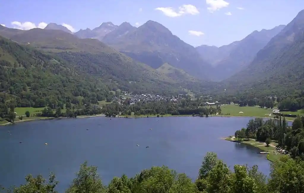 Lac bordé de bois en premier plan et village de Genos en arrière plan au pied des montagnes