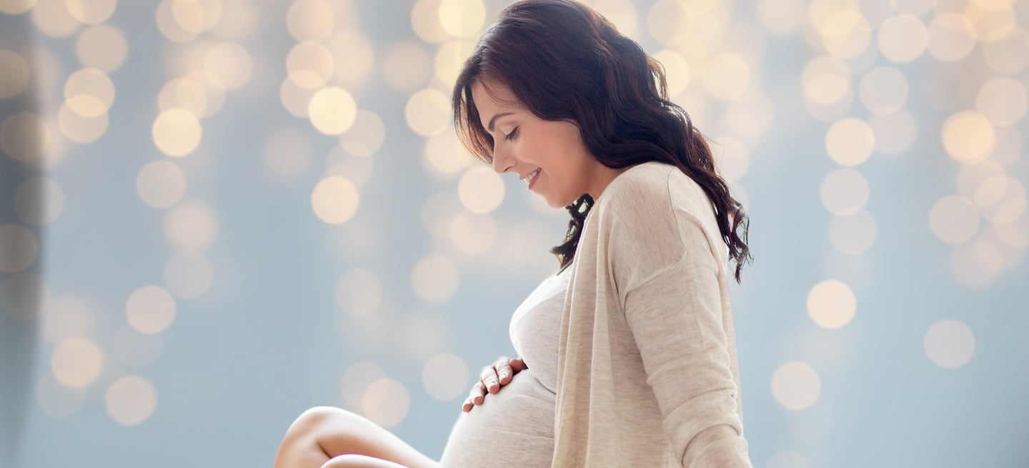 a pregnant woman sitting on a bed with a white dress