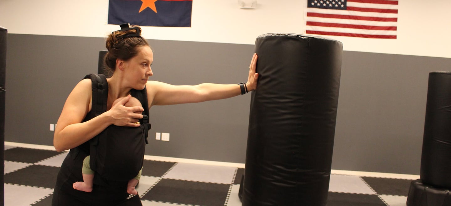 Instructor carrying her baby and striking a heavy bag 