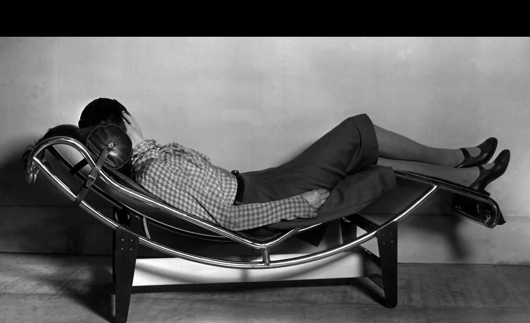 Black and white photo of a person reclining on a modern chaise longue, reflecting Charlotte Perriand