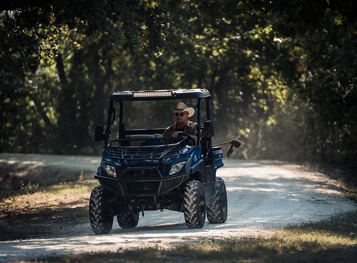 man in cowboy hat driving a huntve utv with a weed trimmer in the back