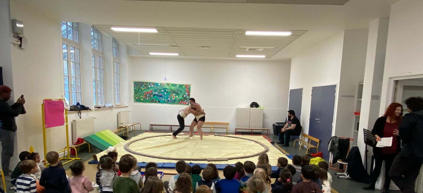 Des enfants regardent 2 hommes lutter sur un dohyo