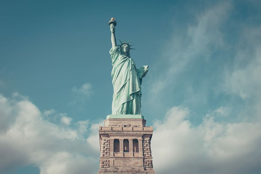 A close-up of the Statue of Liberty, standing tall with her torch raised against a clear blue sky.