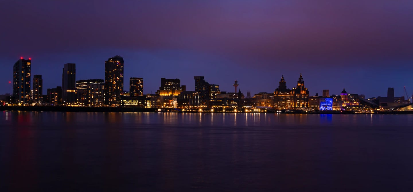 Panoramic Liverpool skyline at night with illuminated buildings reflecting in the River Mersey.