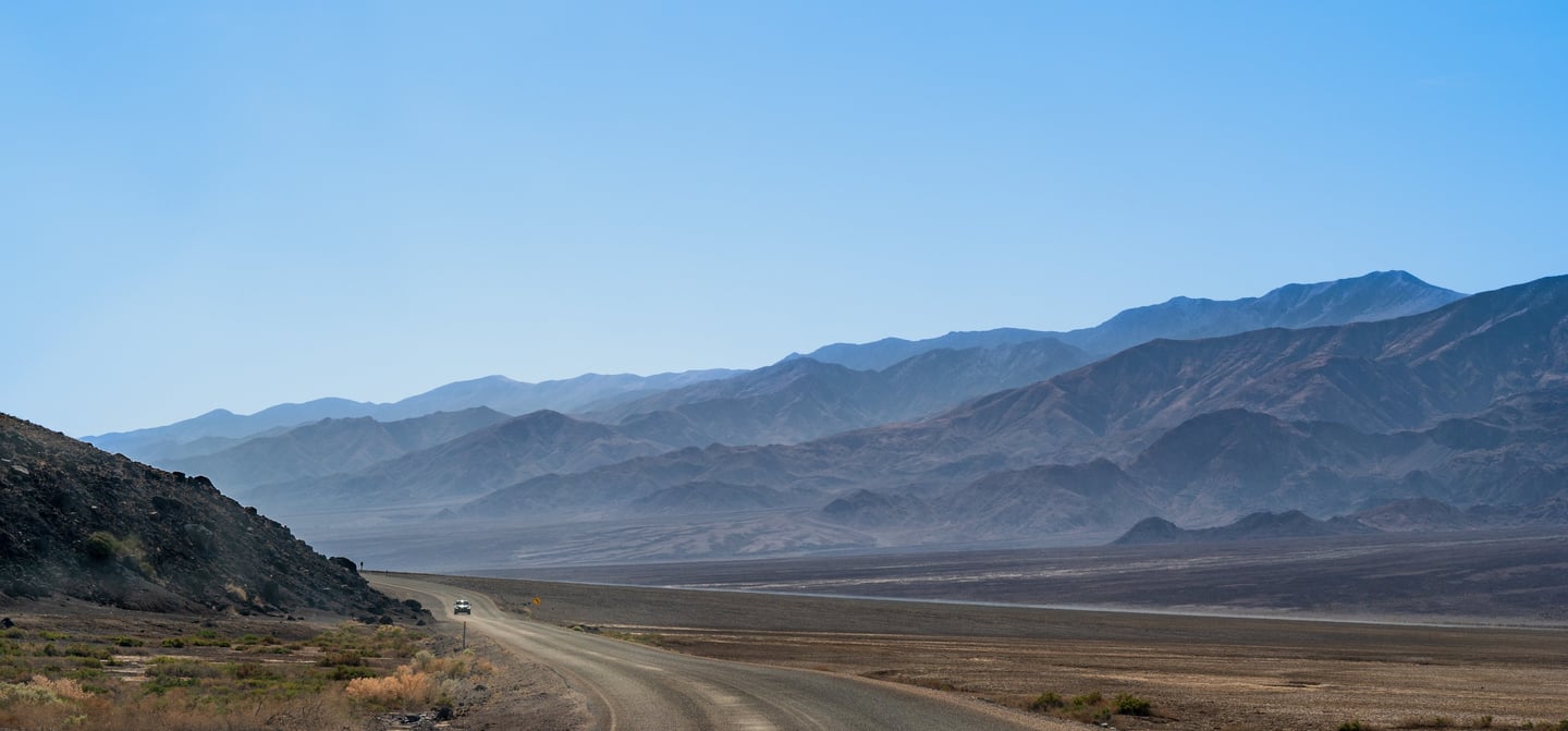 a hazy expanse of mountains intersected by a windy dirt road in death valley california