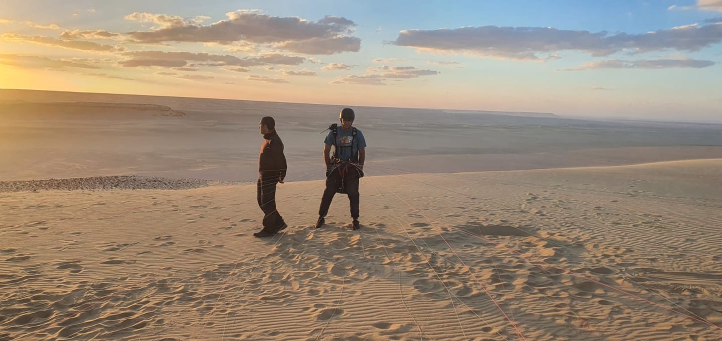 two people standing on a sand dune paragliding egypt