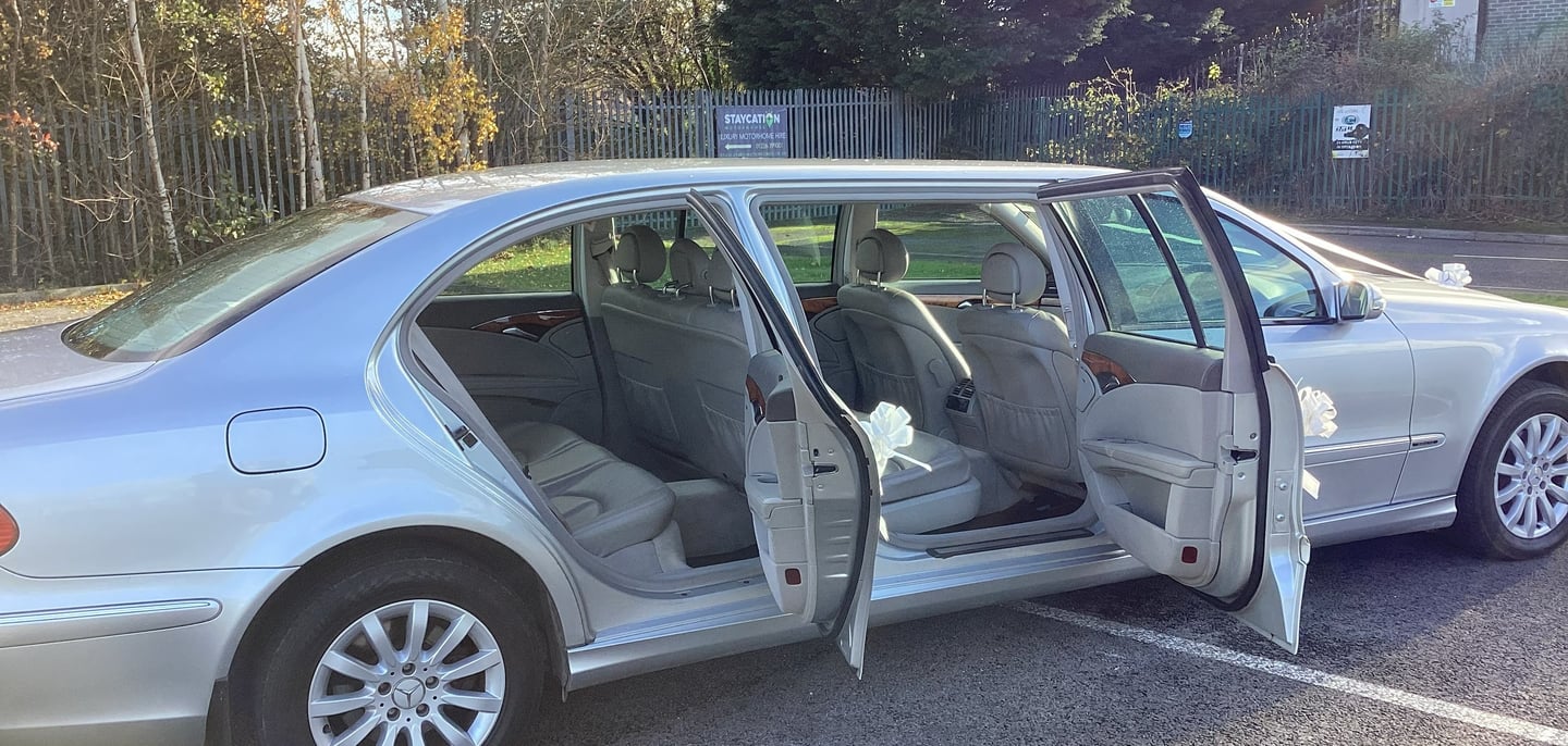 Silver stretch limousine parked in a lot with all four side doors open, revealing a light-colored leather interior.