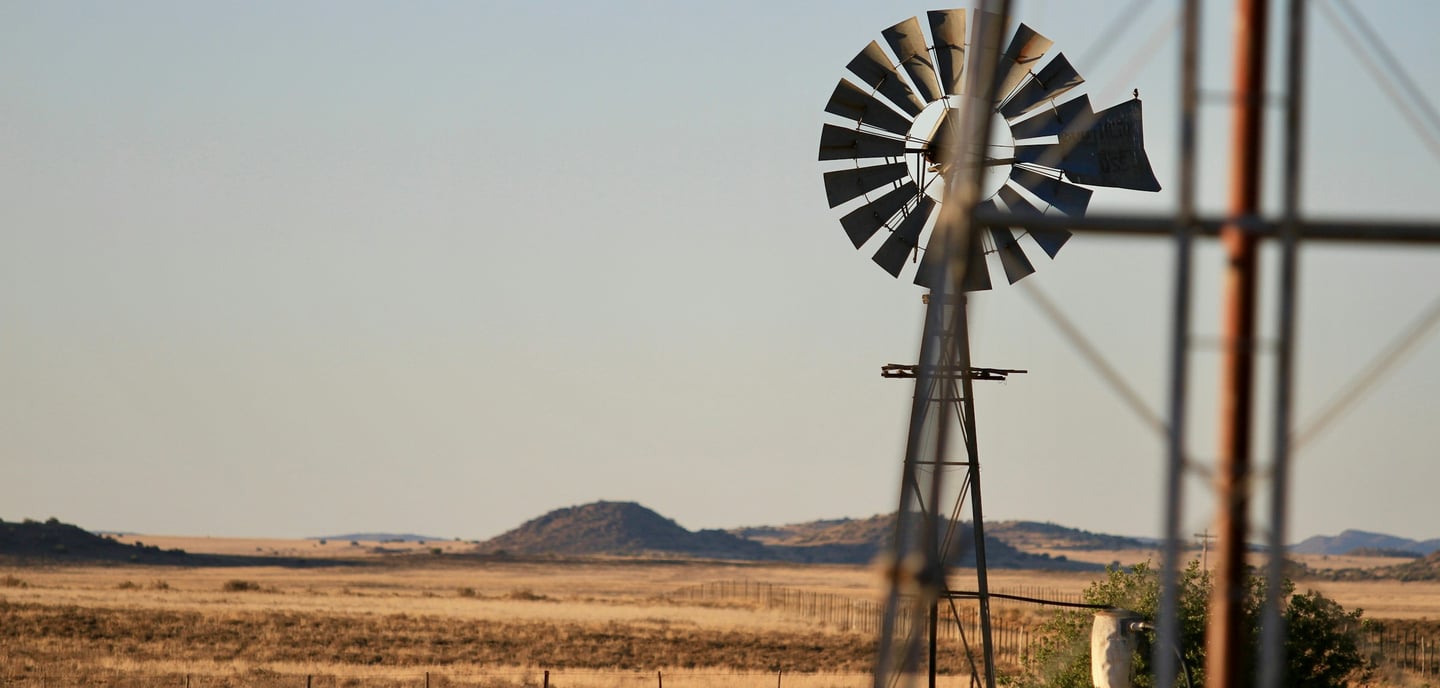 Windmill with trough in the middle of a dry landscape with some hills in the back