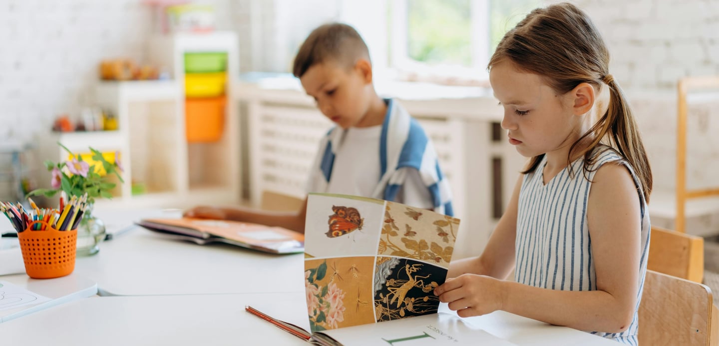 A girl and a boy sit at table reading.