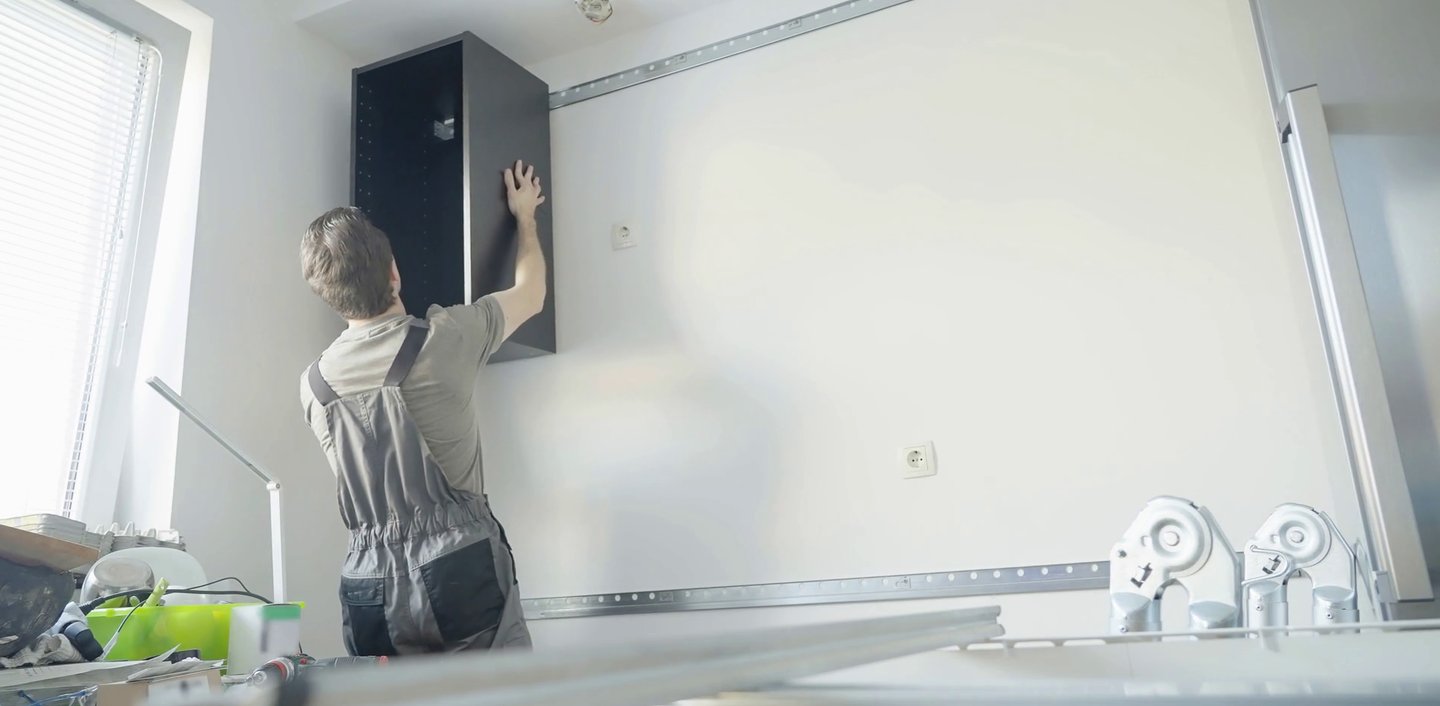 Mężczyzna montuje korpus szafki wiszącej za pomocą listwy montażowej 