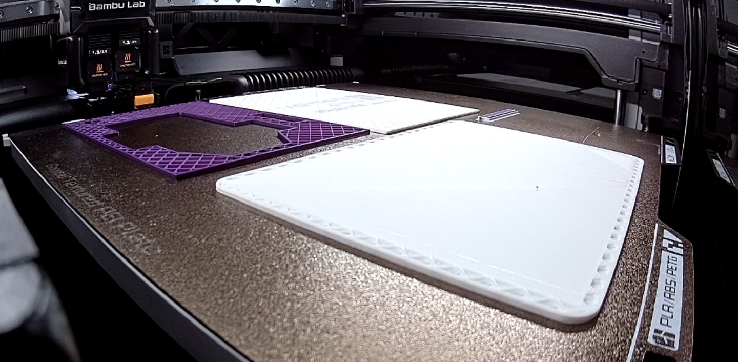 Bambu Lab 3D printer bed with purple and white filament parts being printed.