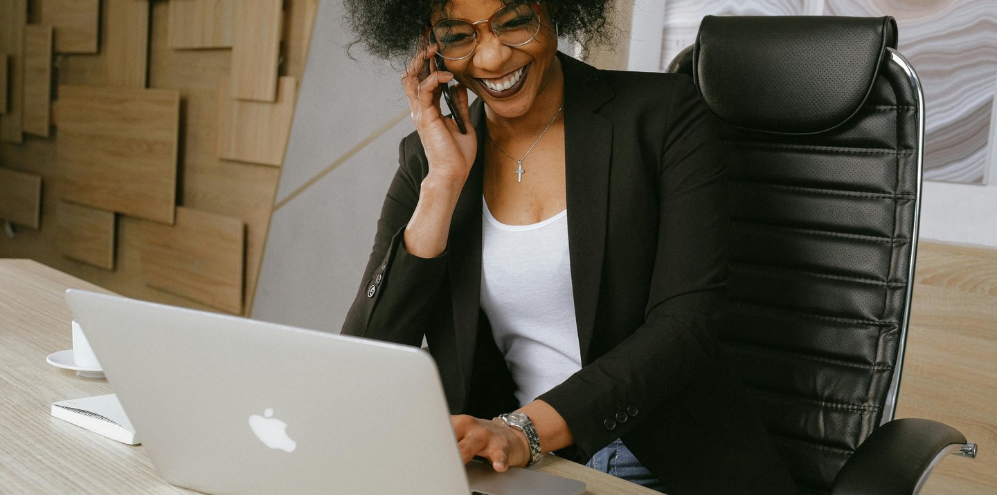 a woman sitting at a desk with a laptop and a cell phone