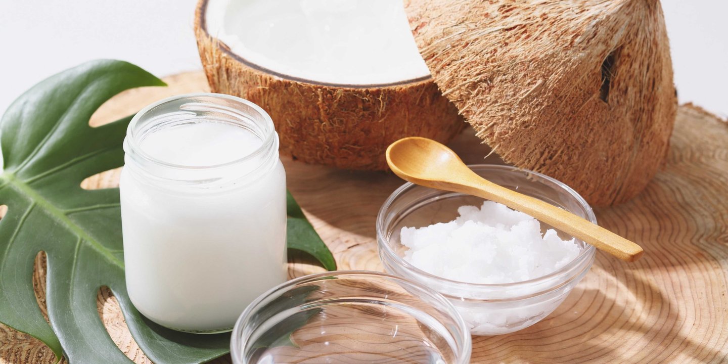 Fotografia de un recipiente de aceite cristalizado de coco junto a unos cocos
