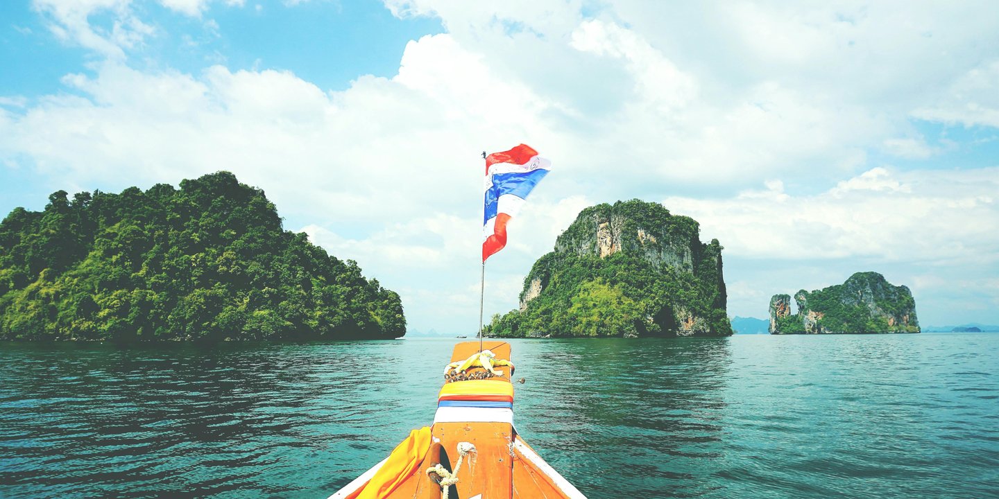 A traditional Thai longtail boat sailing past limestone islands in the tropical waters of Thailand.