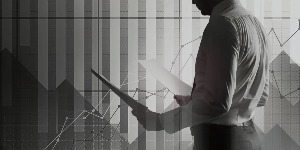 Um empresário analisando relatórios financeiros com gráficos e tabelas de dados ao fundo.