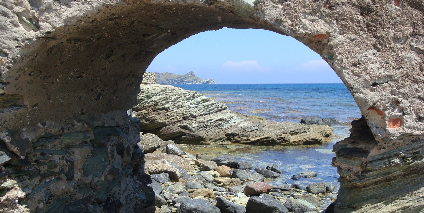 Arcade rocheuse en forme de rond par lequel on aperçoit des rochers et la mer toute bleue
