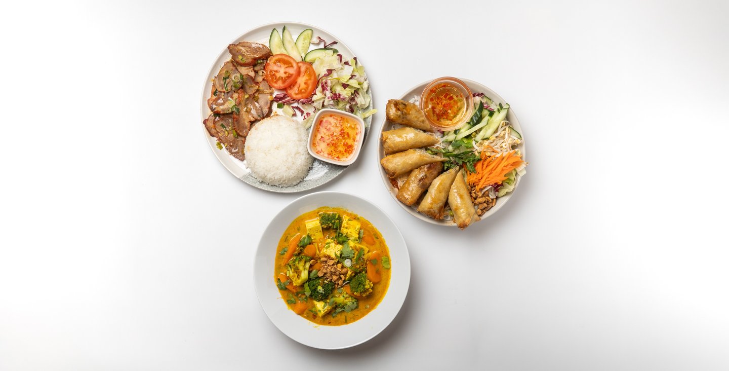 a variety of food items on a table including curry, rice with char siu, and spring roll salad.