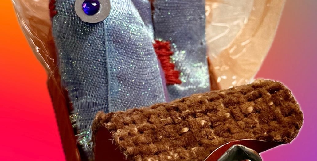 Close-up photo of a sculptor of stitched blue/purple sardine and orange tin with orange foil