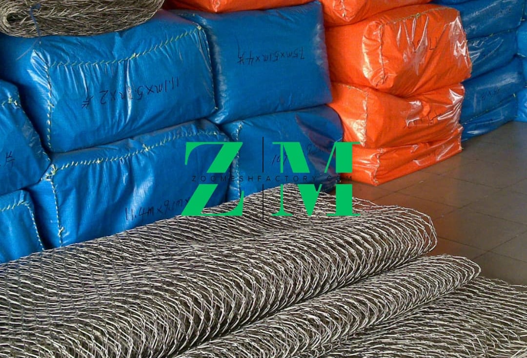 Rolls of stainless steel wire rope mesh in front of orange and blue packaged zoo fencing.