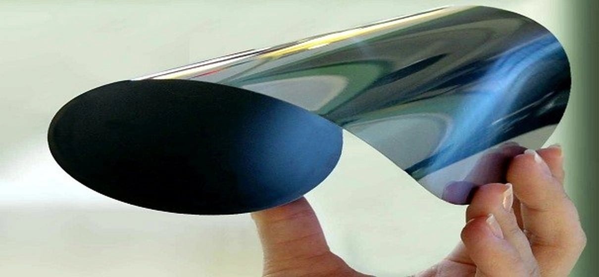 An ultra-thin silicon wafer is shown gently curved, revealing its smooth, reflective surface and ext