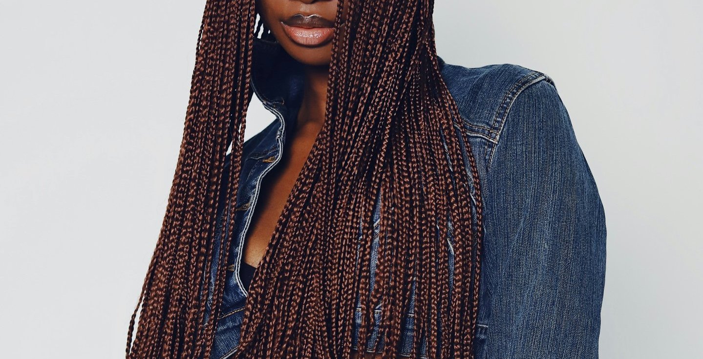 a dark woman with long hair box braids and a denim jacket