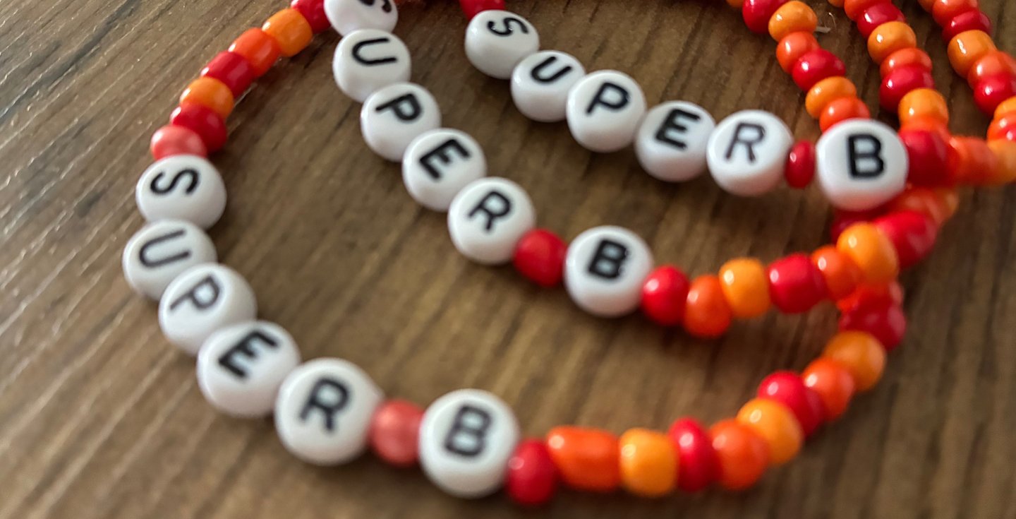 Handmade red and orange beaded friendship bracelets with white letter beads spelling SUPER B.