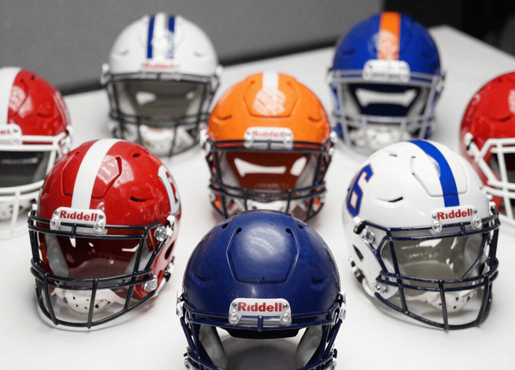 Close-up of a Denver Broncos and Philadelphia Eagles autographed Riddell mini helmet side by side on a wooden display shelf.