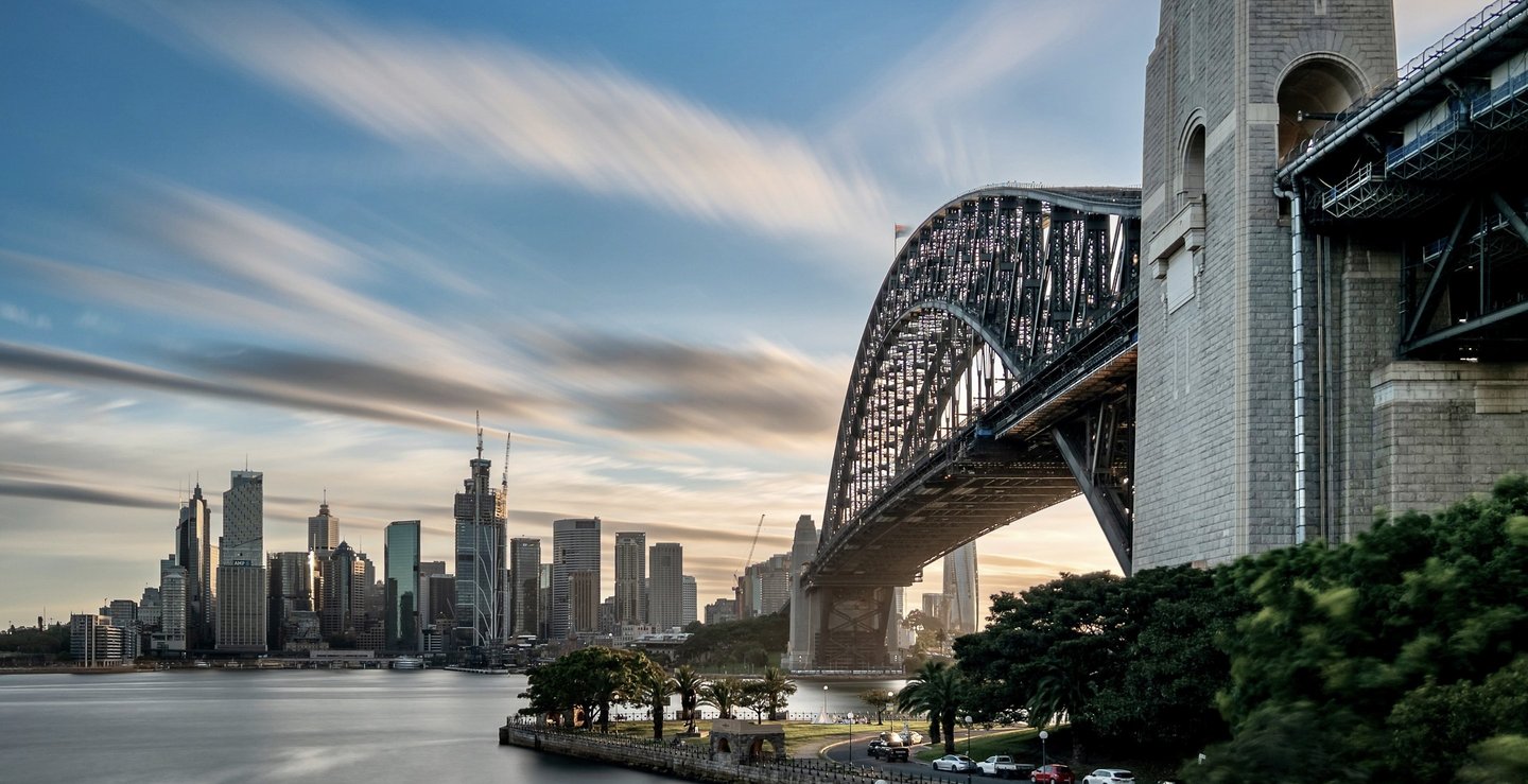 Sydney Harbour Bridge at sunset with a view of the city skyline and moving clouds.