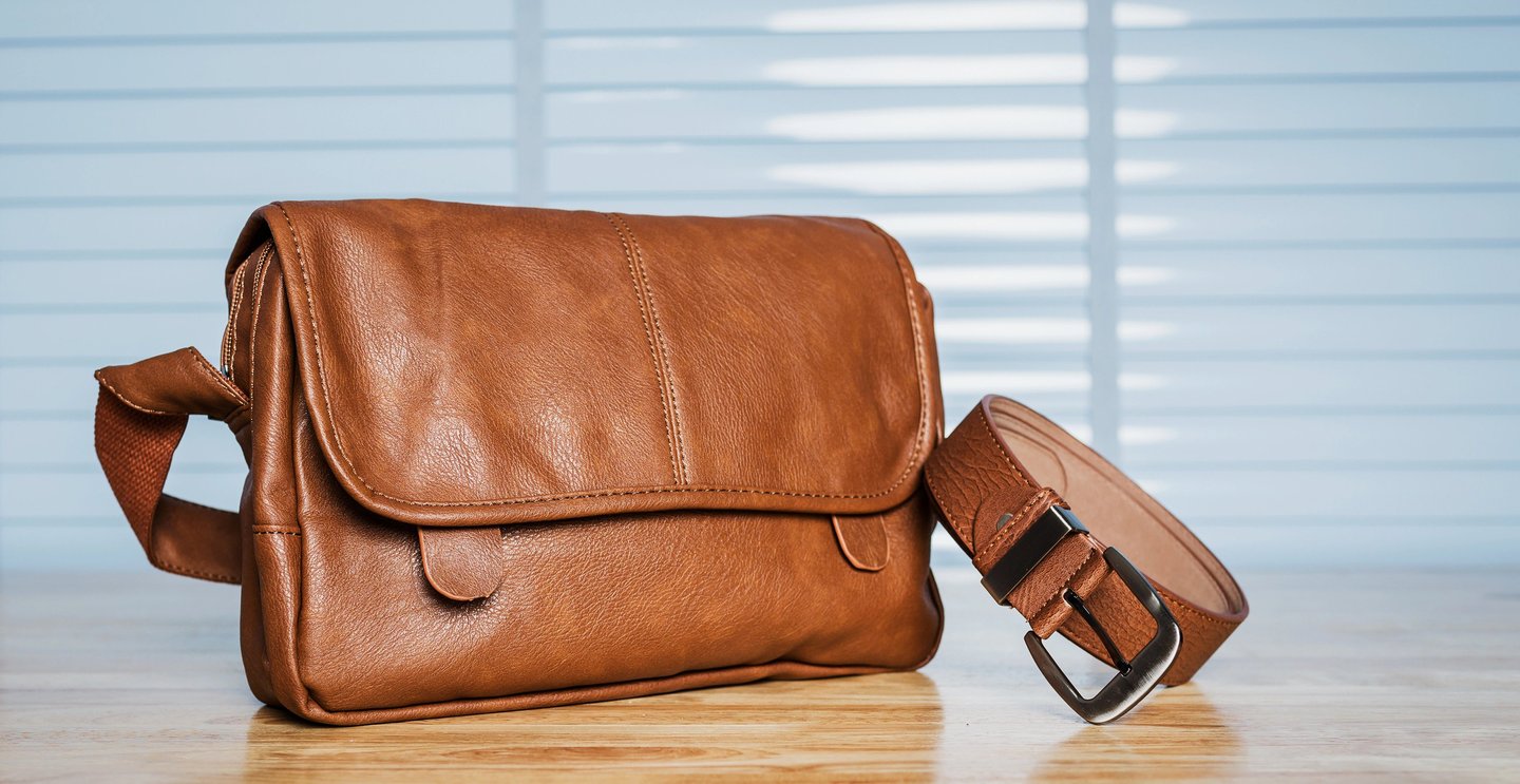 Vintage travelling for men's accessories, brown bag and belt put on modern wooden desk table in the office