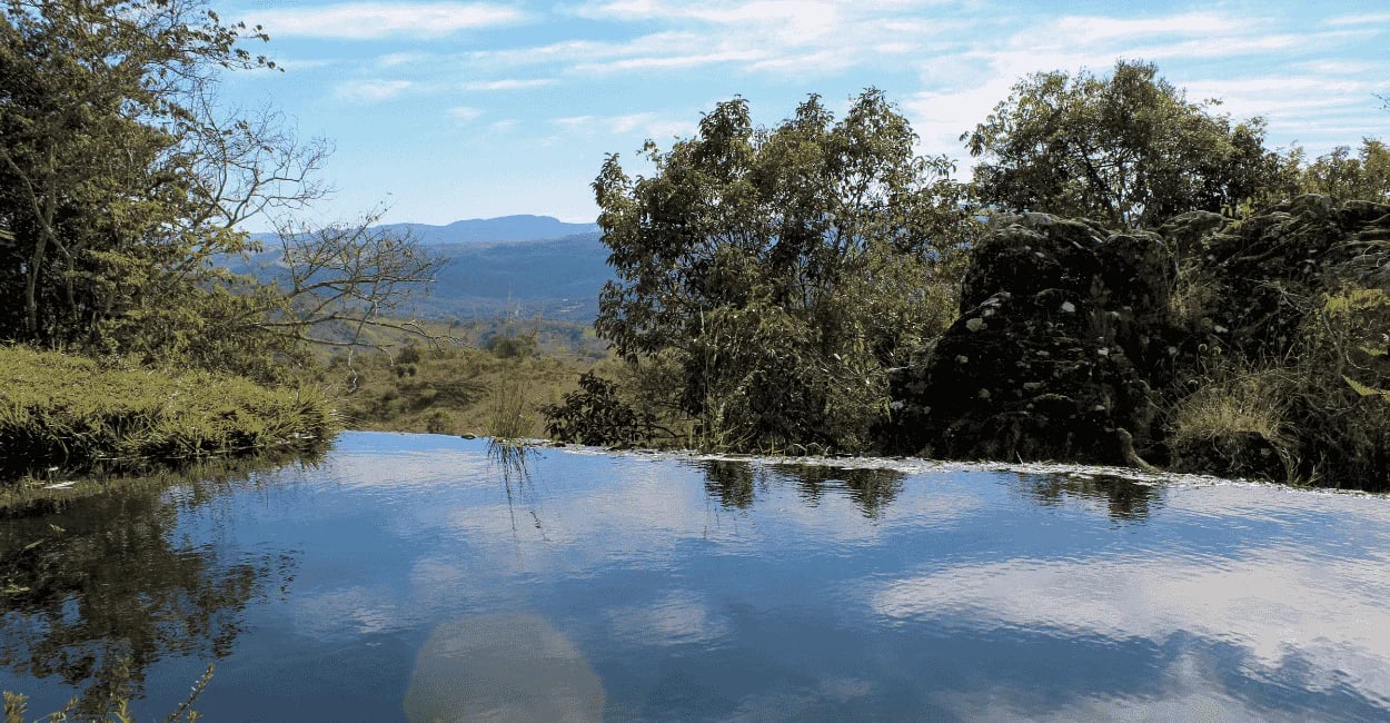 Água refletindo o céu com vista para as montanhas na Cachoeira do Comércio, MG