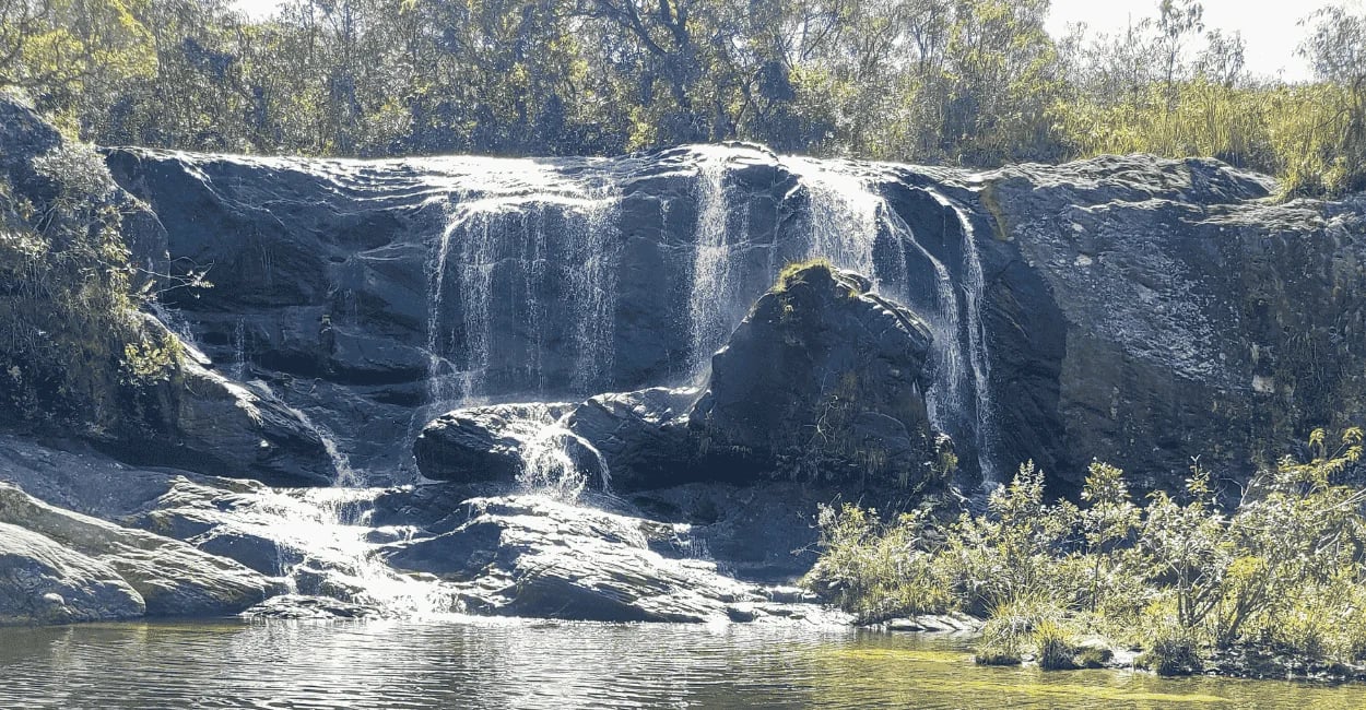 Cachoeira do Leão com pequenas quedas d’água sobre pedras escuras e poço raso em meio à vegetação