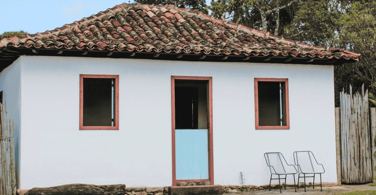 Casa simples com telhado colonial, porta azul e cadeiras na área externa em Chapada, Ouro Preto