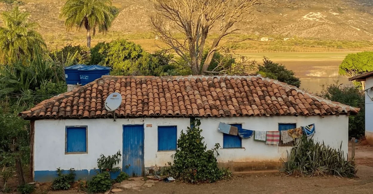 Casa simples em Lapinha da Serra, com janelas azuis, telhado de barro e paisagem rural ao fundo
