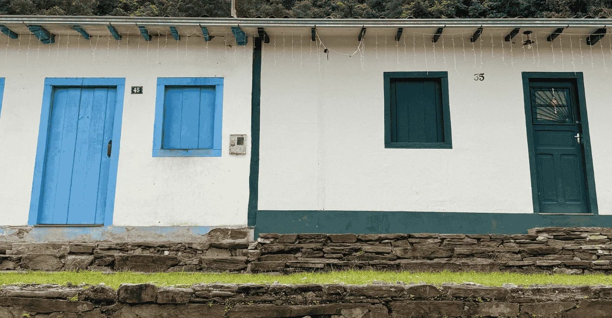 Casario colonial em Brumal MG, com portas e janelas azuis, parede branca e calçamento de pedra