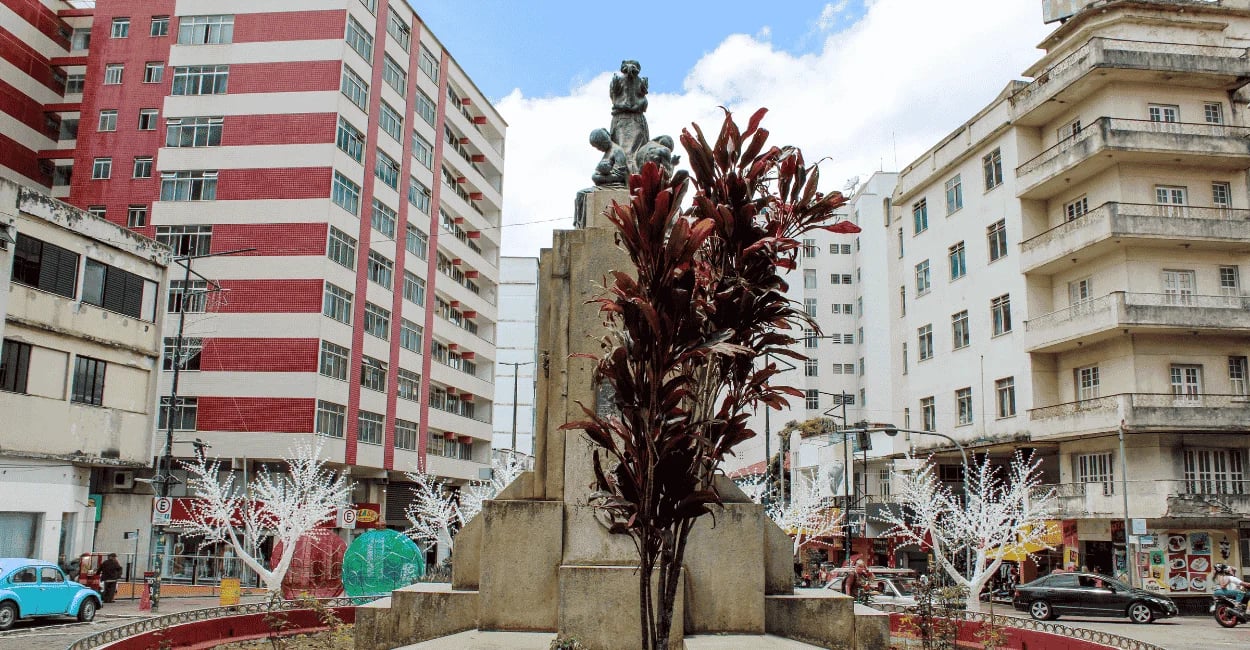 Praça central de Barbacena, com uma árvore, monumento e prédios em Minas Gerais