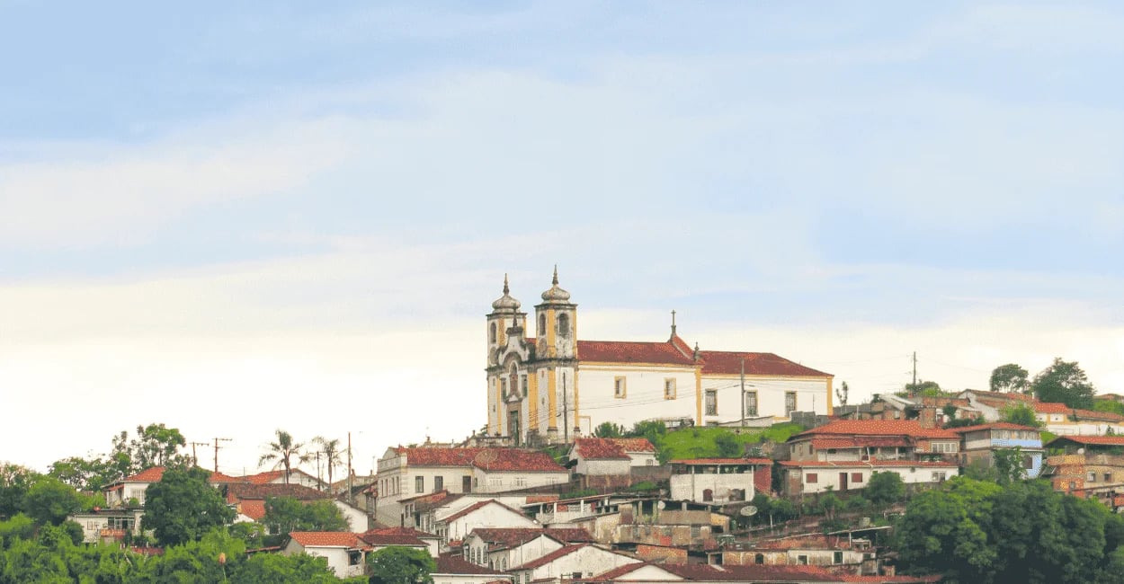Vista distante de Ouro Preto com igreja histórica, casario colonial e céu claro ao fundo