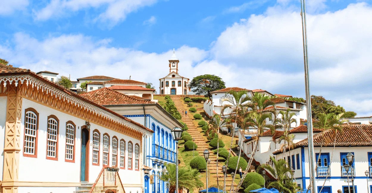 Escadaria da Igreja de Santa Rita no Serro MG com casario colonial, jardins e céu azul ao fundo