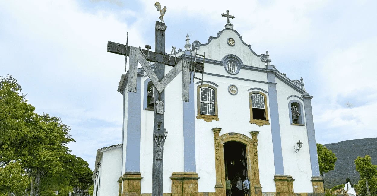 Igreja da Santissima Trindade com cores brancas e azul claro, com uma cruz de madeira a frente