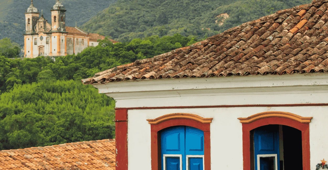 Casarão de Ouro Preto em primeiro plano e vista para igreja cercada por montanhas verdes