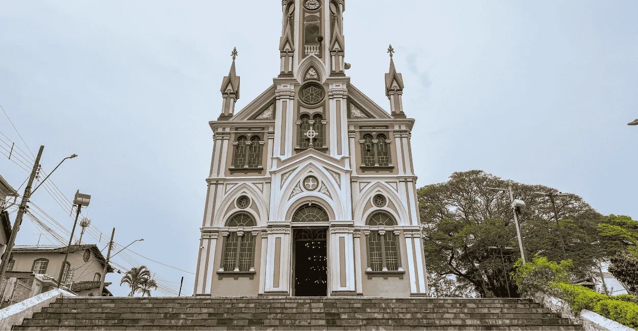 Fachada de igreja neogótica em tons de marrom e branco vista de escadaria em Entre Rios de Minas