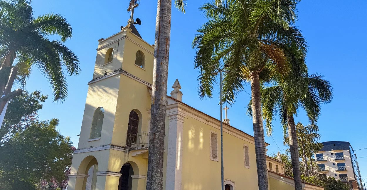 Igreja Matriz de Itatiaiuçu cercada por palmeiras sob céu azul em Minas Gerais